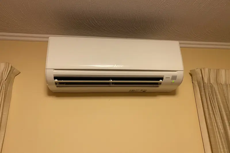 Slim white ductless indoor unit mounted high on a beige wall between two curtain panels